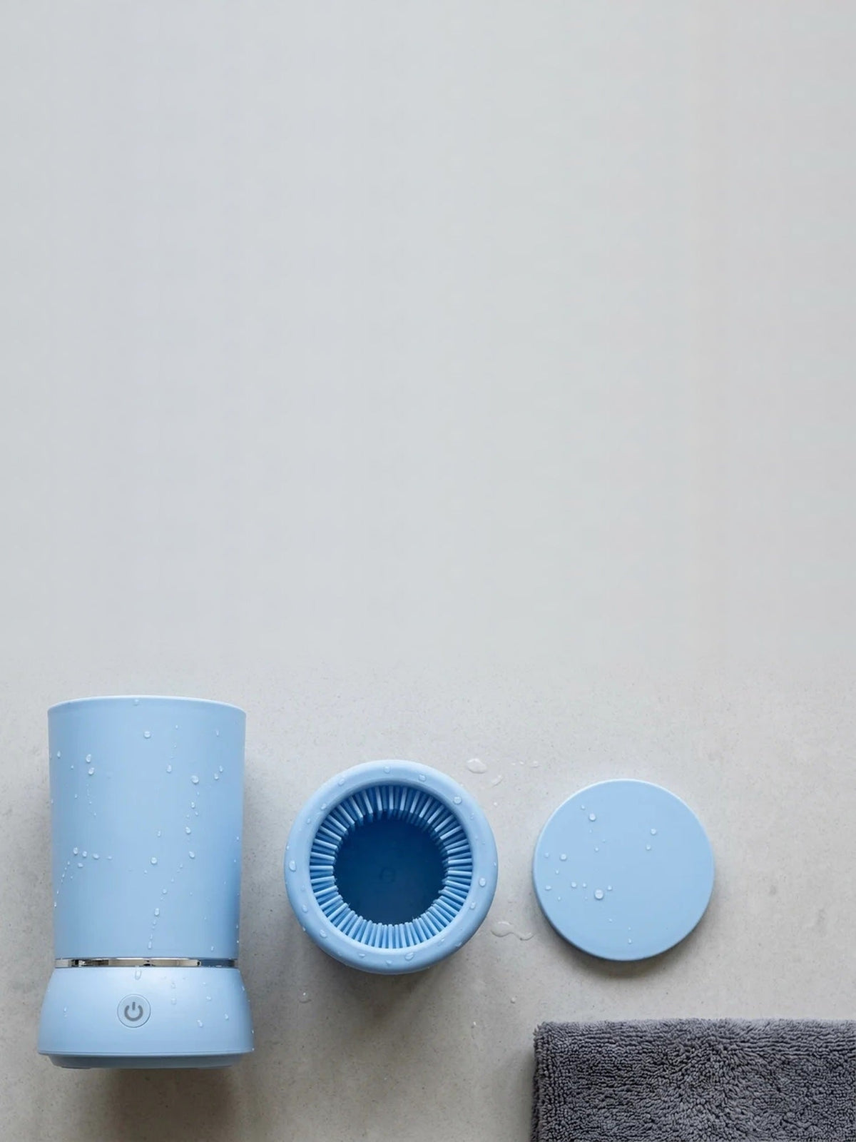 PawWash automatic paw cleaner in blue, shown with the removable silicone brush insert and lid on a pale concrete surface